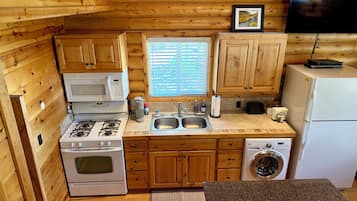 A compact kitchen with wooden cabinets, a microwave, stove, sink, and a washing machine.
