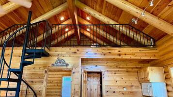 Ein Interieur einer Holzhütte mit einer Wendeltreppe, einer Holztür, einem kleinen Tisch und einem Kühlschrank.