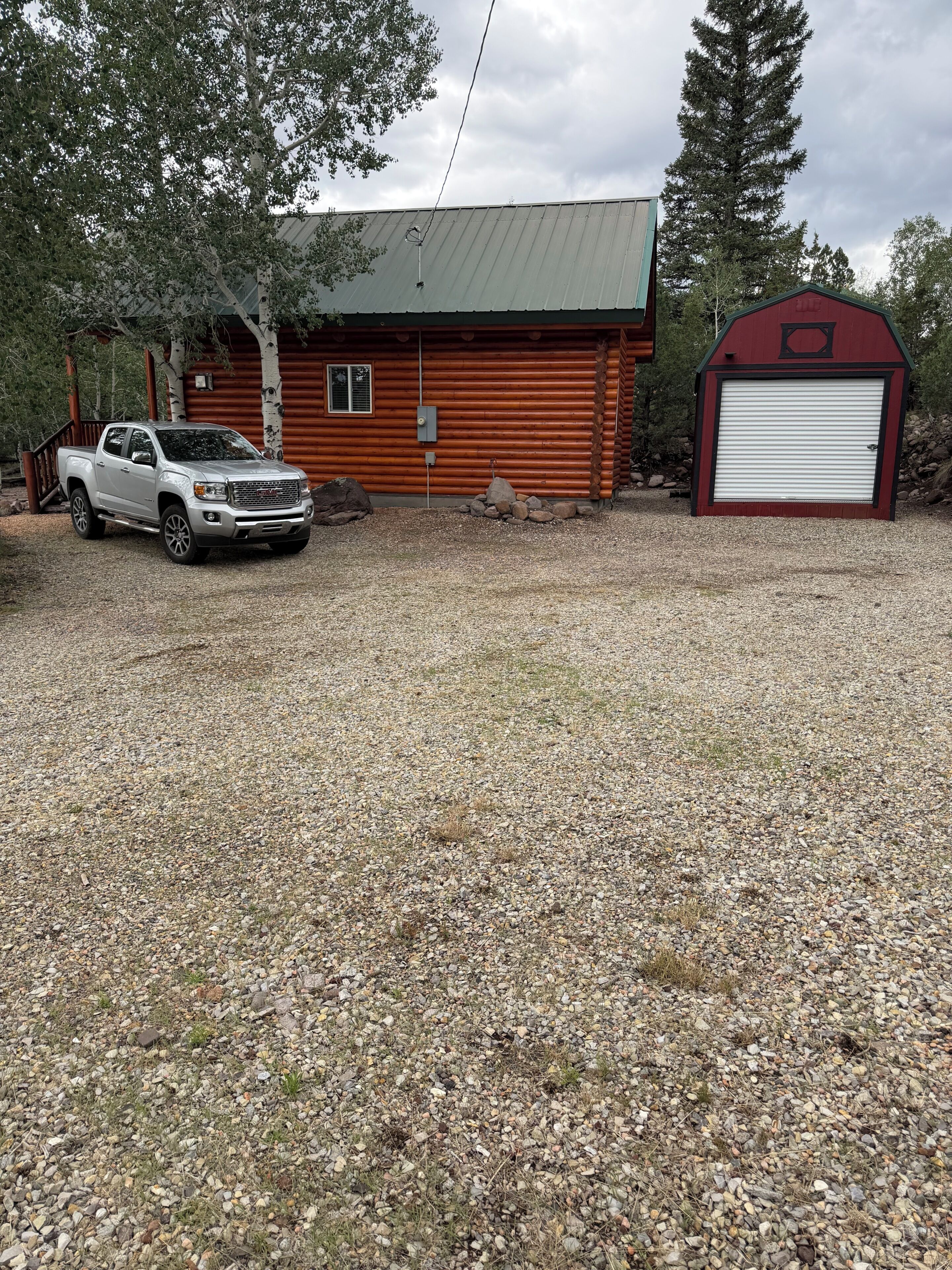 Mökki, jonka edessä on sorapäällysteinen ajotie, valkoinen lava-auto on parkissa sen edessä ja oikealla puolella on punainen lato.