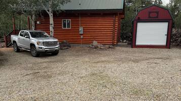 Mökki, jonka edessä on sorapäällysteinen ajotie, valkoinen lava-auto on parkissa sen edessä ja oikealla puolella on punainen lato.