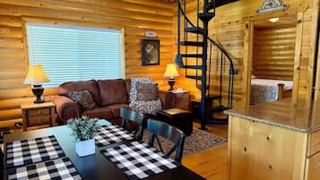 A cozy cabin interior with a wooden interior, a sofa, a dining table with checkered placemats, and a spiral staircase.