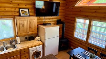 A log cabin interior with a kitchen, a washing machine, a dining table, and a television mounted on the wall.