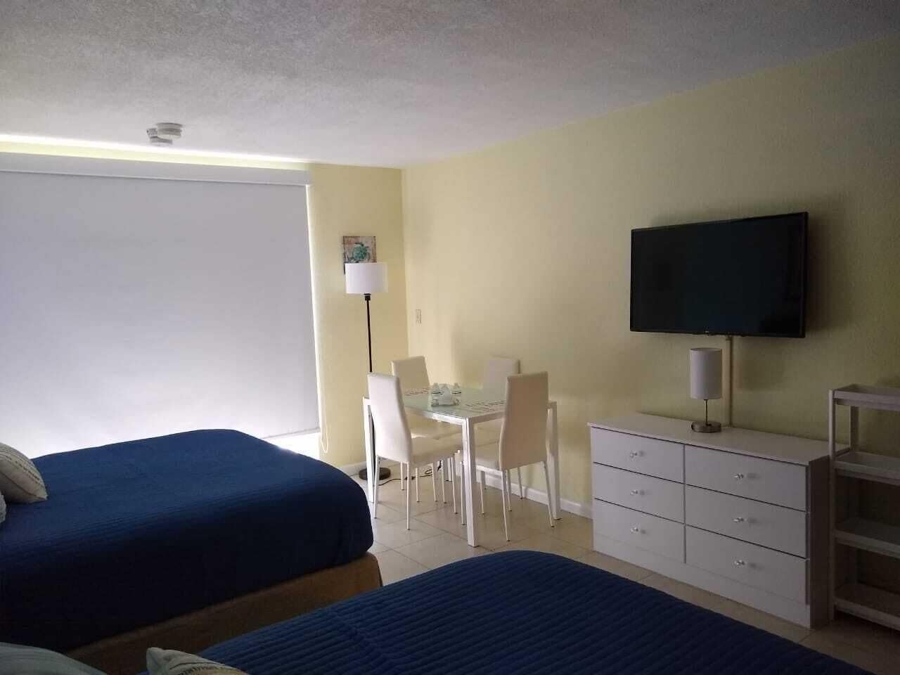 A hotel room with two beds, a desk, a chair, a television, and a cabinet.