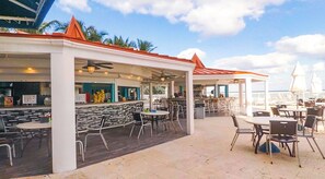 An outdoor patio area with tables and chairs, a bar area with stools, and a view of the ocean. - Hermoso estudio para 4 personas con balcon y vista al mar STR02214 (Sunny Isles Beach)