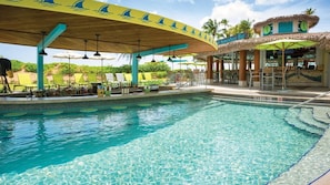 A pool area with a covered seating area, lounge chairs, and a bar.