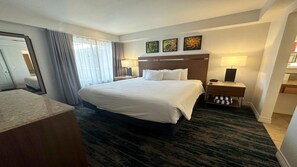 Ein Hotelzimmer mit einem großen Bett, zwei Nachttischen, einem Spiegel und Blick ins Freie.