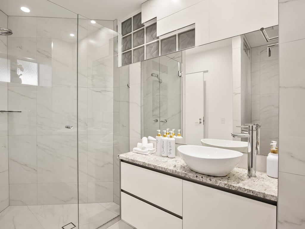 A modern bathroom with a glass shower enclosure, a white sink, and a large mirror.