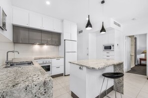 Una cucina moderna con mobili bianchi, piani di lavoro in granito, cappa aspirante in acciaio inossidabile e lampada a sospensione nera.