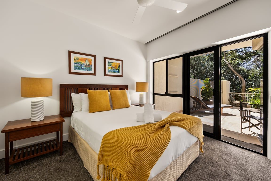A hotel room with a bed, two bedside lamps, a nightstand, a large window, and a view of the outdoors.
