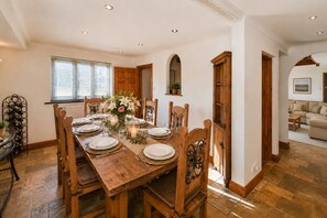 A dining area with a wooden table set for six, surrounded by chairs, with a vase of flowers and candles on the table.