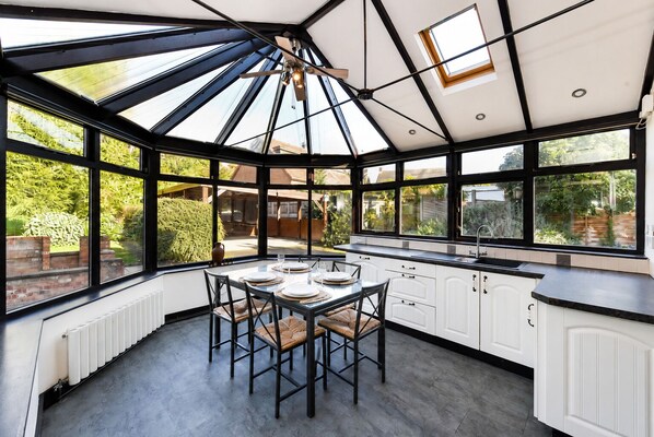 A conservatory with a dining table set for four, surrounded by white cabinetry and large windows.