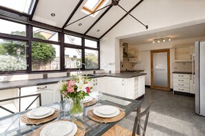 A modern kitchen with a glass dining table set for four, a large window, and a view of the outdoors.