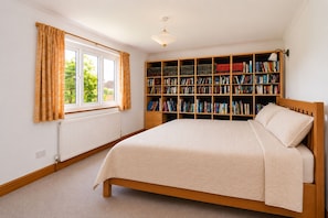 Ein Schlafzimmer mit einem großen Bett, einem Bücherregal, einem Fenster mit Vorhängen und einer Heizung.