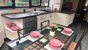 A modern kitchen with a glass dining table set for four, featuring pink plates and a potted plant. - The Old Farmhouse - six-bedroom house in rural village for up to twelve guests. (Nottingham)