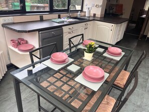 Eine moderne Küche mit einem Glastisch für vier Personen, ausgestattet mit rosa Tellern und einem Blumentopf.