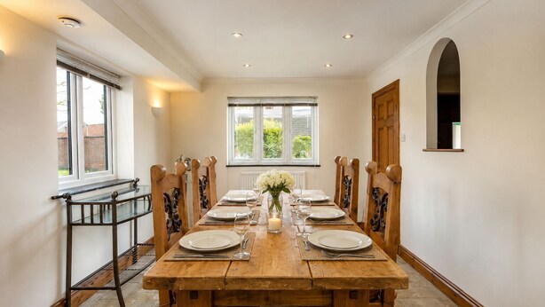A dining room with a long wooden table set for six, flanked by chairs with carved wooden backs. - The Old Farmhouse - six-bedroom house in rural village for up to twelve guests. (Nottingham)