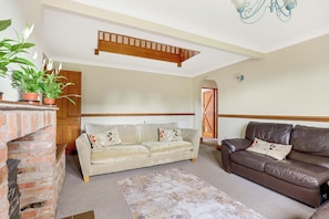 A living room with a sofa, a brown leather couch, a brick fireplace, and a staircase.