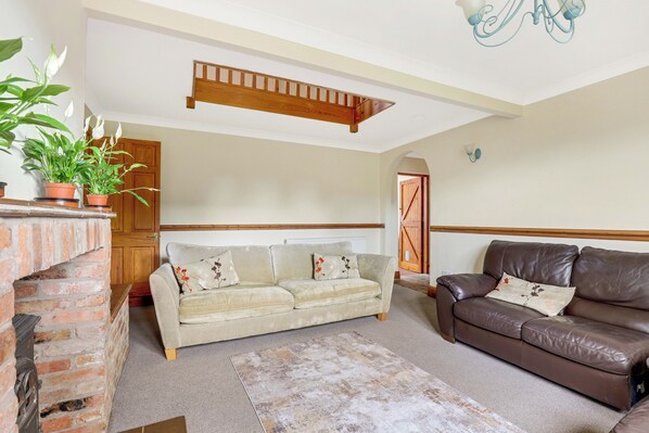 A living room with a sofa, a brown leather couch, a brick fireplace, and a staircase.