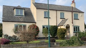 A two-story house with a sloped roof, multiple windows, and a front entrance. - The Old Farmhouse - six-bedroom house in rural village for up to twelve guests. (Nottingham)