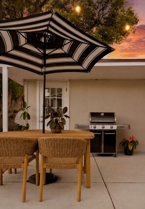 Un patio exterior con una mesa, sillas, una parrilla y una sombrilla.