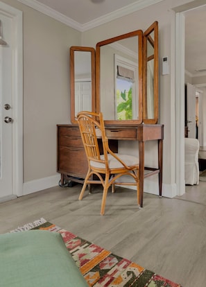 Ein Zimmer mit Holztisch, Stuhl, Spiegel, Kommode und einem gemusterten Teppich.