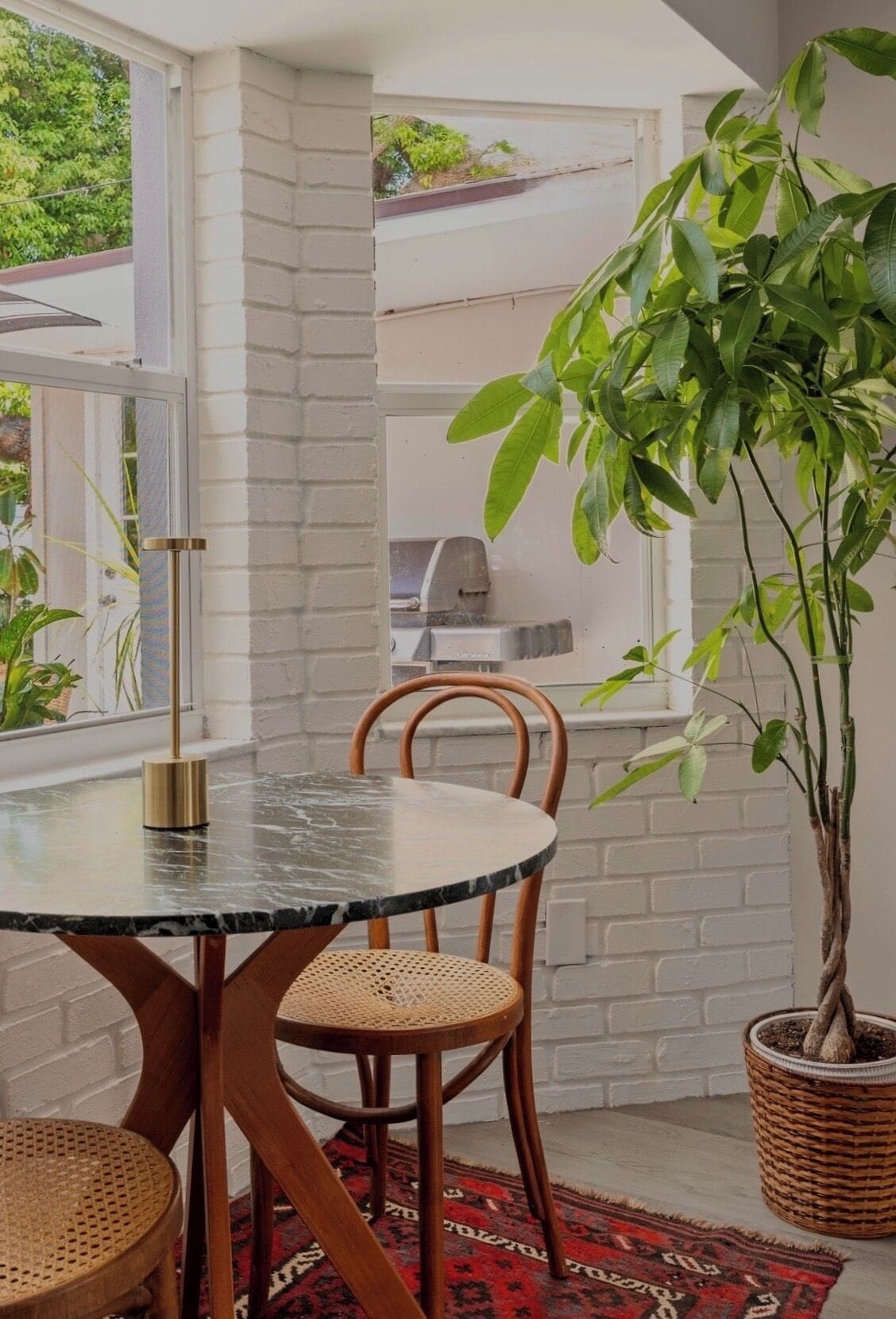 A dining area with a round table, two chairs, a potted plant, and a brick wall.
