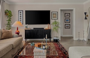 Ein Wohnzimmer mit Sofa, Couchtisch, Fernseher, einer Pflanze und gerahmten Bildern an der Wand.