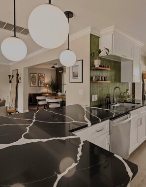 Una cocina moderna con encimera de mármol negro, armarios blancos e iluminación colgante.