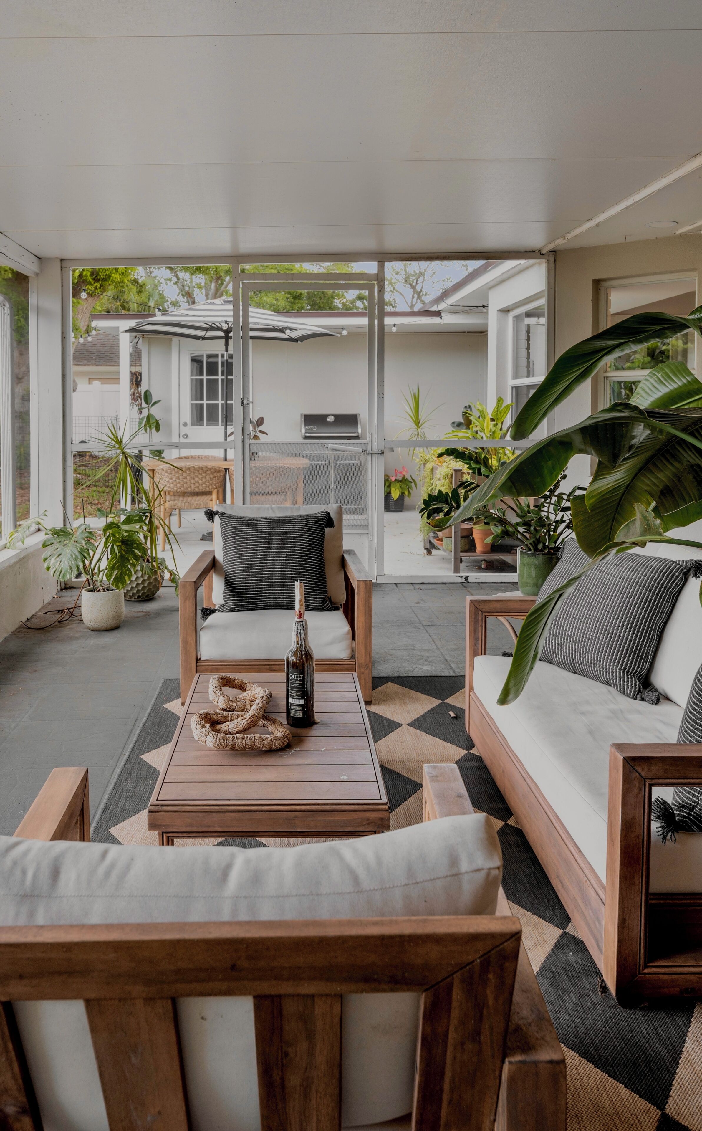 Un espace extérieur abrité avec des sièges, une table en bois, une bouteille et un barbecue en arrière-plan.