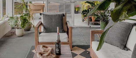 Un área de estar al aire libre con techo, una mesa de madera, una botella y una parrilla al fondo.