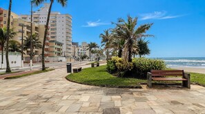 Ein gepflasterter Weg mit Bänken, Palmen und Blick aufs Meer.