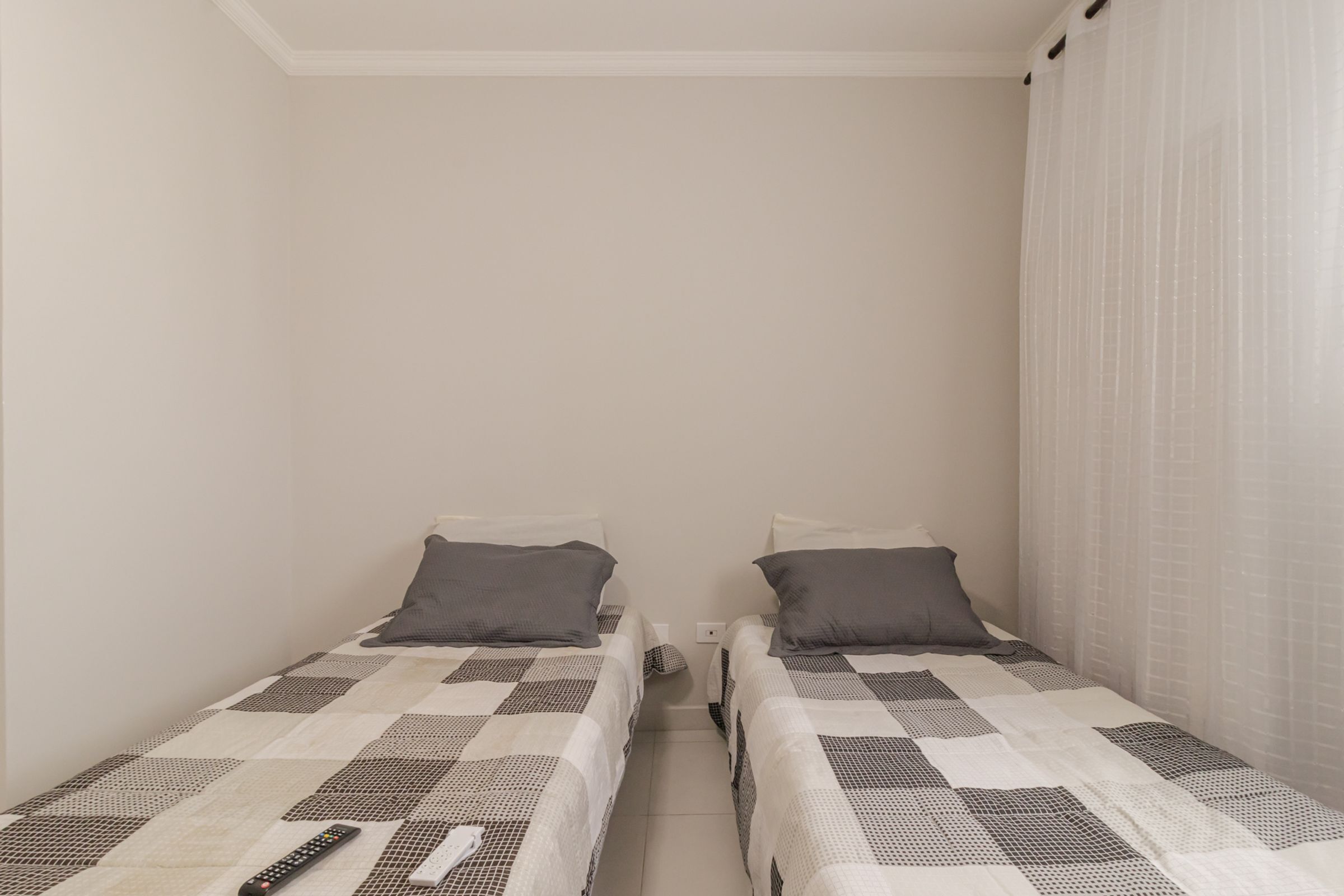 Een kleine accommodatie met één kamer en twee eenpersoonsbedden, elk met een kussen en dekbed.