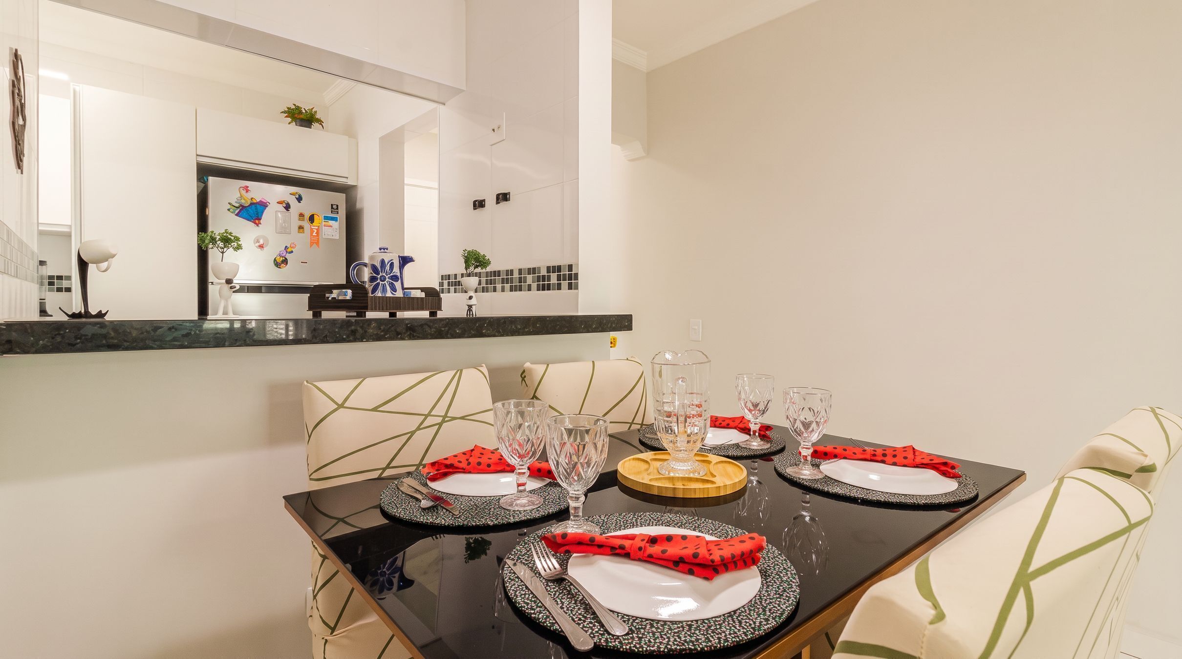 Un coin repas avec une table noire dressée pour quatre personnes, des assiettes blanches, des serviettes rouges et de la verrerie transparente.