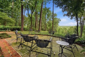 Eine Terrassengruppe im Freien mit Metallstühlen und einem Tisch, umgeben von Bäumen und Grünpflanzen.