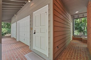 Eine Garage mit Überdachung, zwei weißen Türen, einem Backsteinboden und einer Holzfassade.