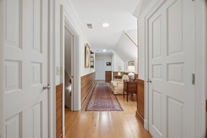 Ein Korridor mit Holzboden, weißen Türen, einem gemusterten Teppich und einer Sitzecke mit einer Lampe.