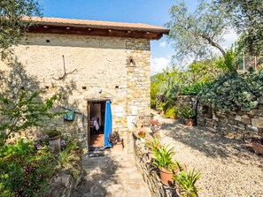 A stone building with a tiled roof, a doorway, and a garden with various plants and flowers. - Viletta Ulivo by Interhome (Diano Marina)