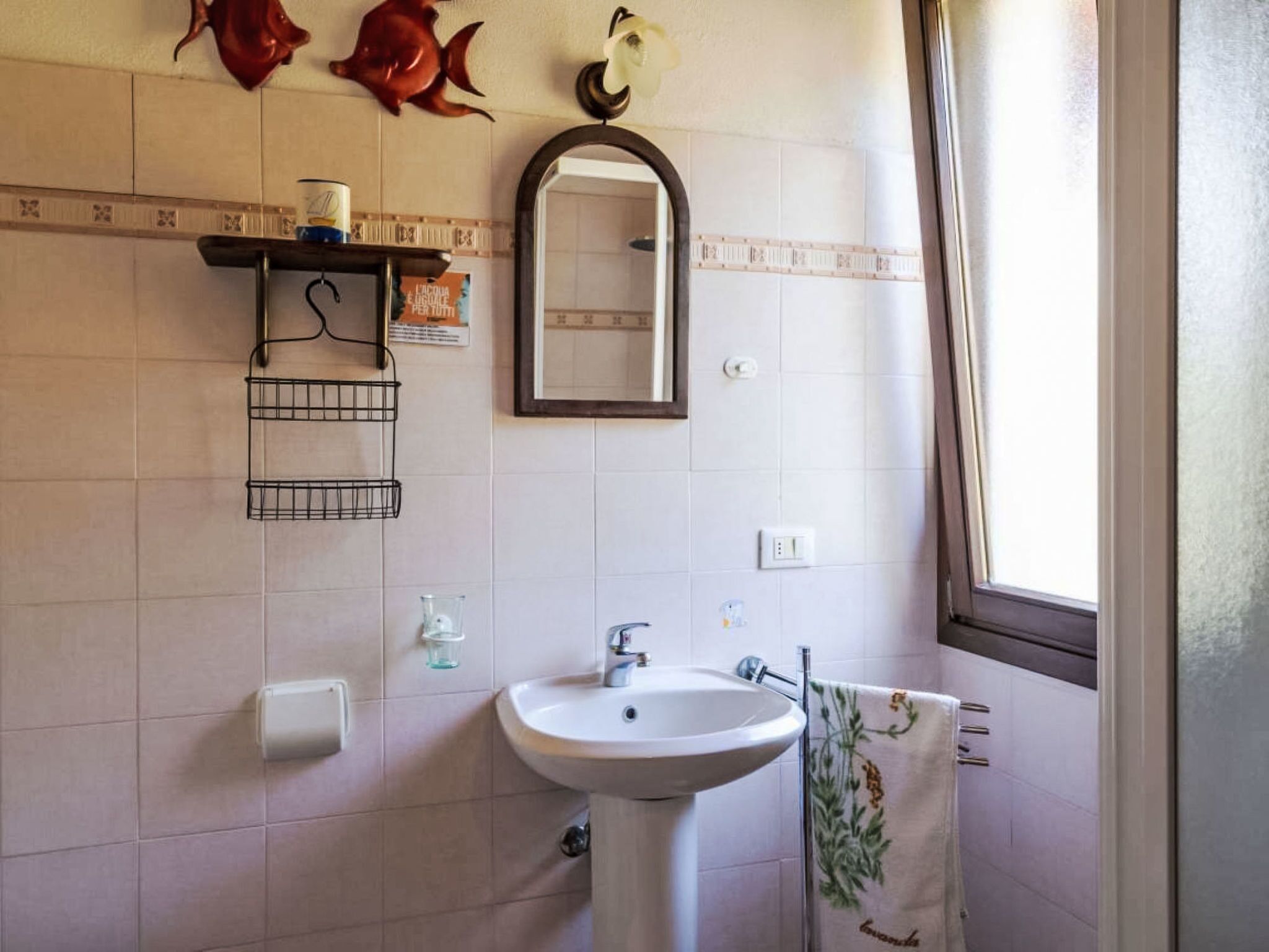 A bathroom with a sink, mirror, towel rack, and decorative fish on the wall.
