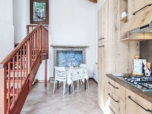 Eine Küche mit einer Holztreppe, einem Esstisch mit Stühlen, einem Kamin und einem Herd.
