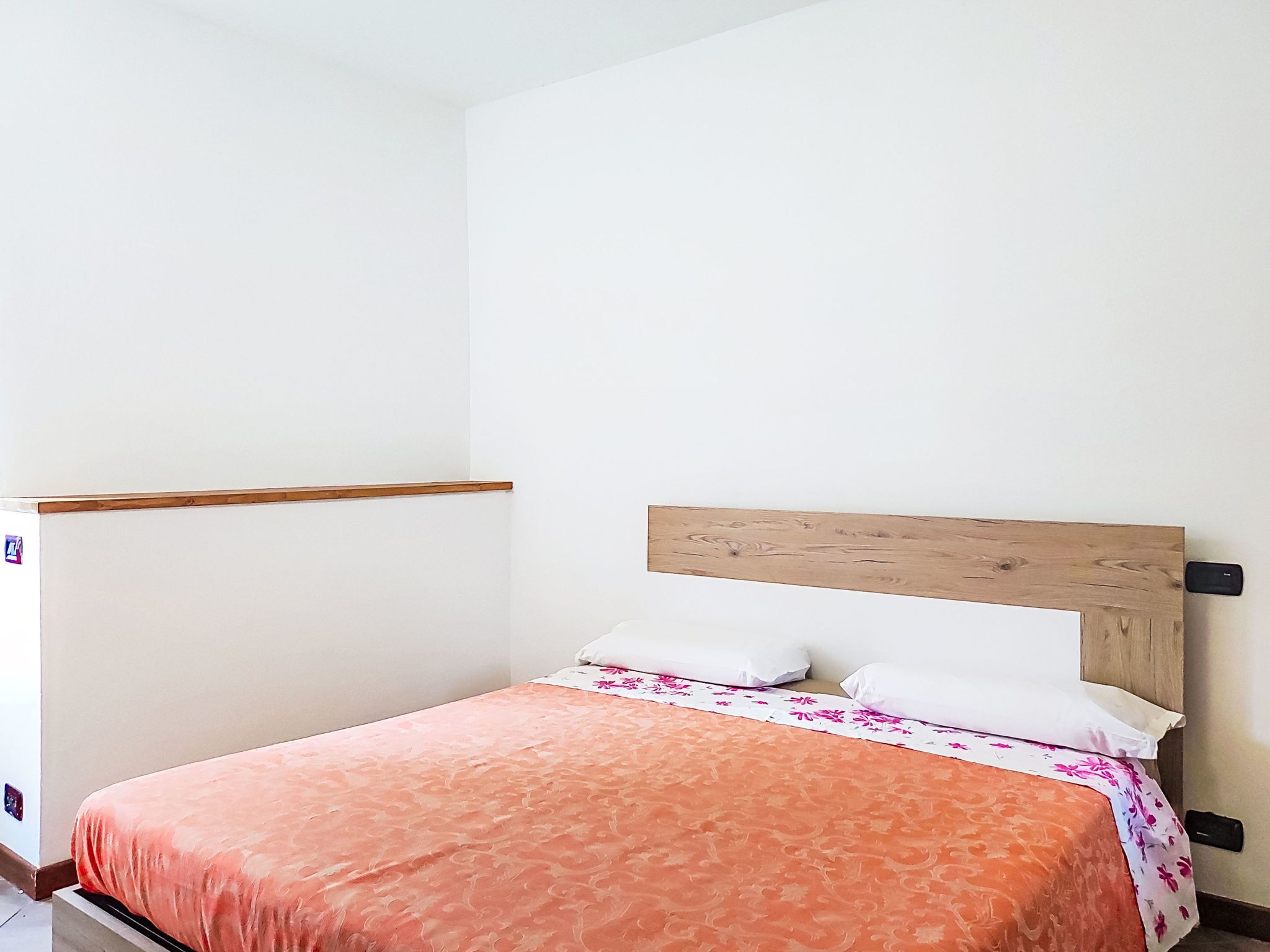 Un lit simple avec une tête de lit en bois, des oreillers blancs et une couvre-lit à motifs orange.