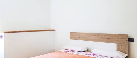 A single bed with a wooden headboard, white pillows, and an orange patterned bedspread.