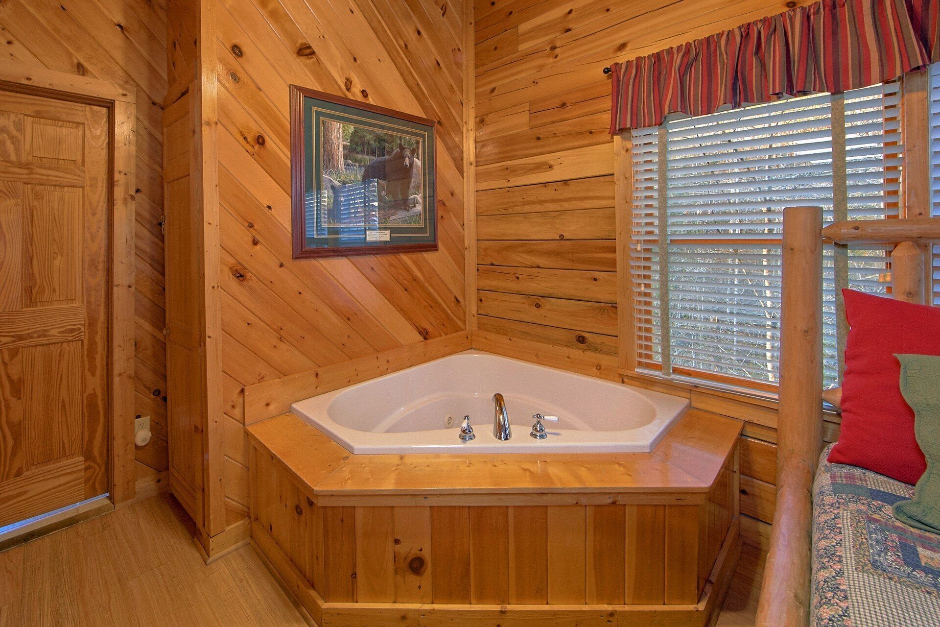 L’intérieur d’un chalet en bois, avec une grande baignoire en bois, un tableau encadré au mur et une fenêtre avec des stores.