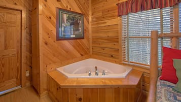 L’intérieur d’un chalet en bois, avec une grande baignoire en bois, un tableau encadré au mur et une fenêtre avec des stores.