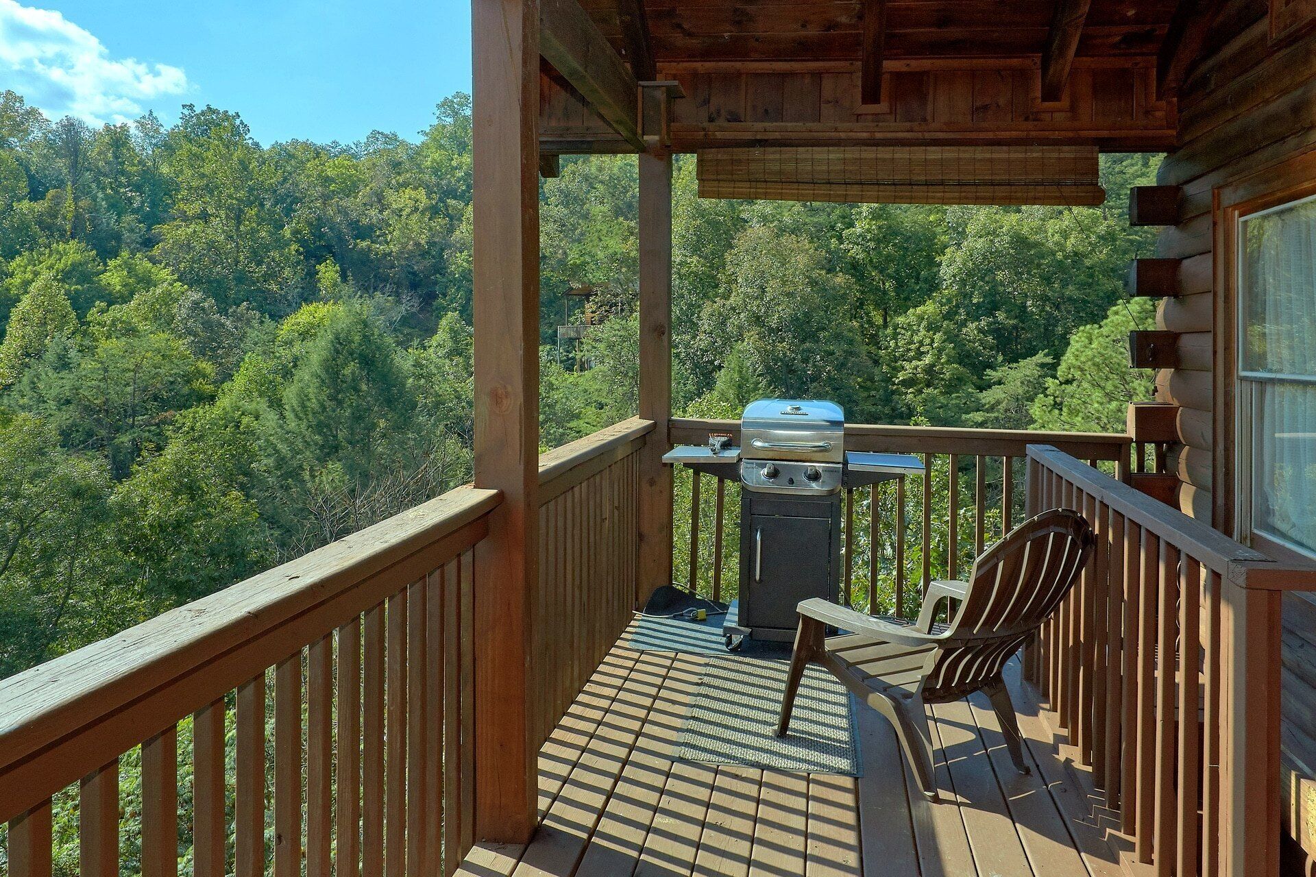 Une terrasse en bois avec un barbecue et une chaise, donnant sur une zone boisée.
