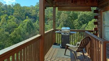 Une terrasse en bois avec un barbecue et une chaise, donnant sur une zone boisée.