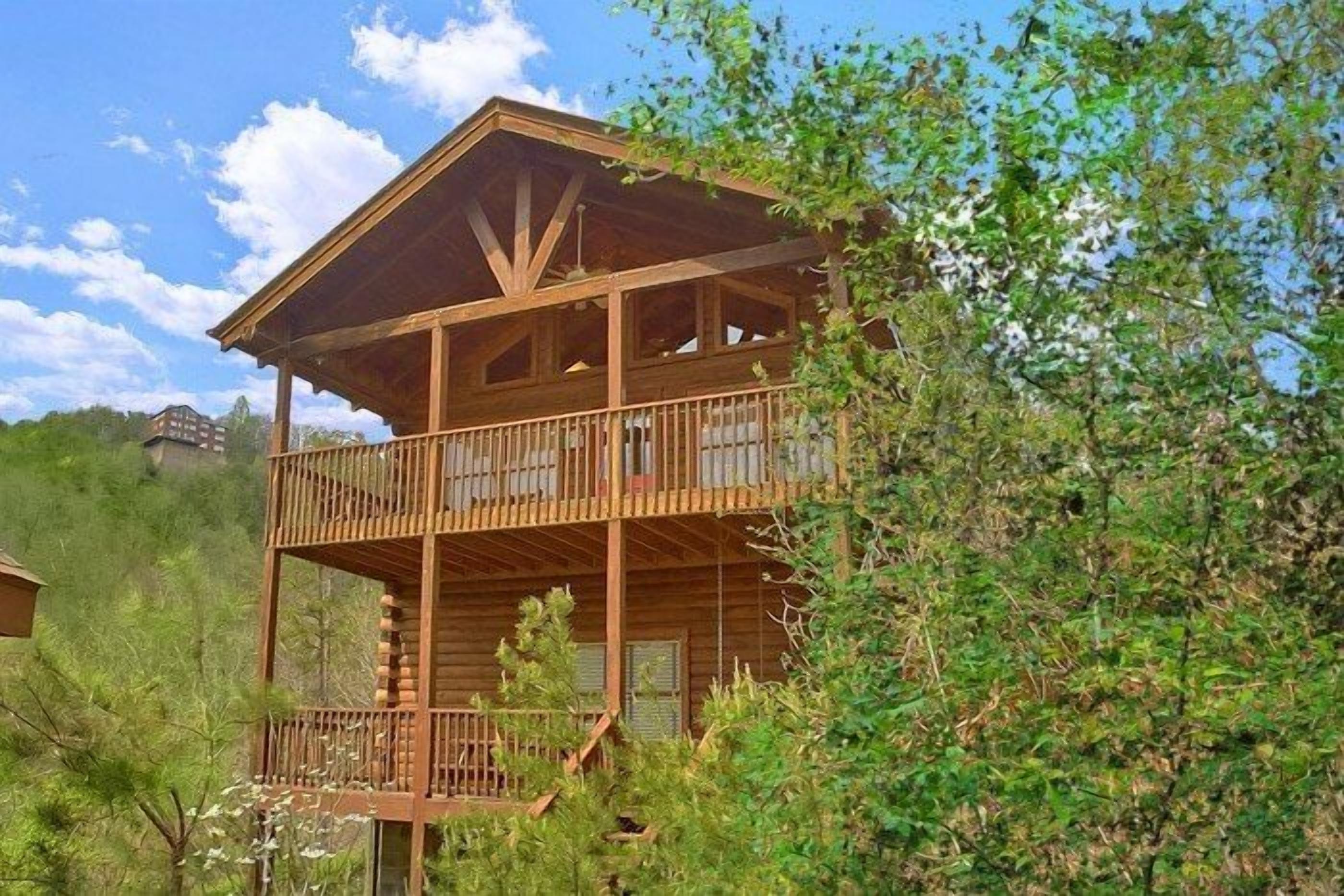 A two-story wooden cabin with a balcony, surrounded by greenery.