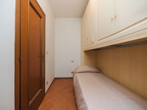 A narrow room with a wooden door, a bed with a headboard, and a white wardrobe. - La Casa di Margot by Interhome (Viareggio)