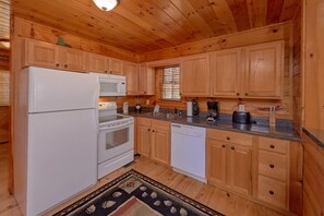 Eine Küche mit Holzausstattung, einem Kühlschrank, einer Mikrowelle, einem Backofen, einem Geschirrspüler und einer Kaffeemaschine.