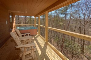 Eine Holzterrasse mit Whirlpool und Stühlen mit Blick auf einen Wald.