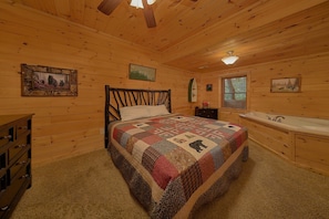 Ein Schlafzimmer einer Holzhütte mit Bett, Schminktisch und einem Badezimmer mit Waschbecken und Fenster.